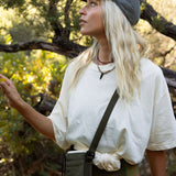 Woman in outdoor setting wearing a white shirt, green shorts, and a cap.