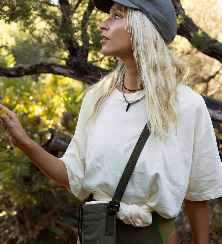 Woman in outdoor setting wearing a white shirt, green shorts, and a cap.